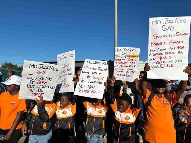 Community members mourn two teen girls in KwaNobuhle with candles and flowers at a memorial site.